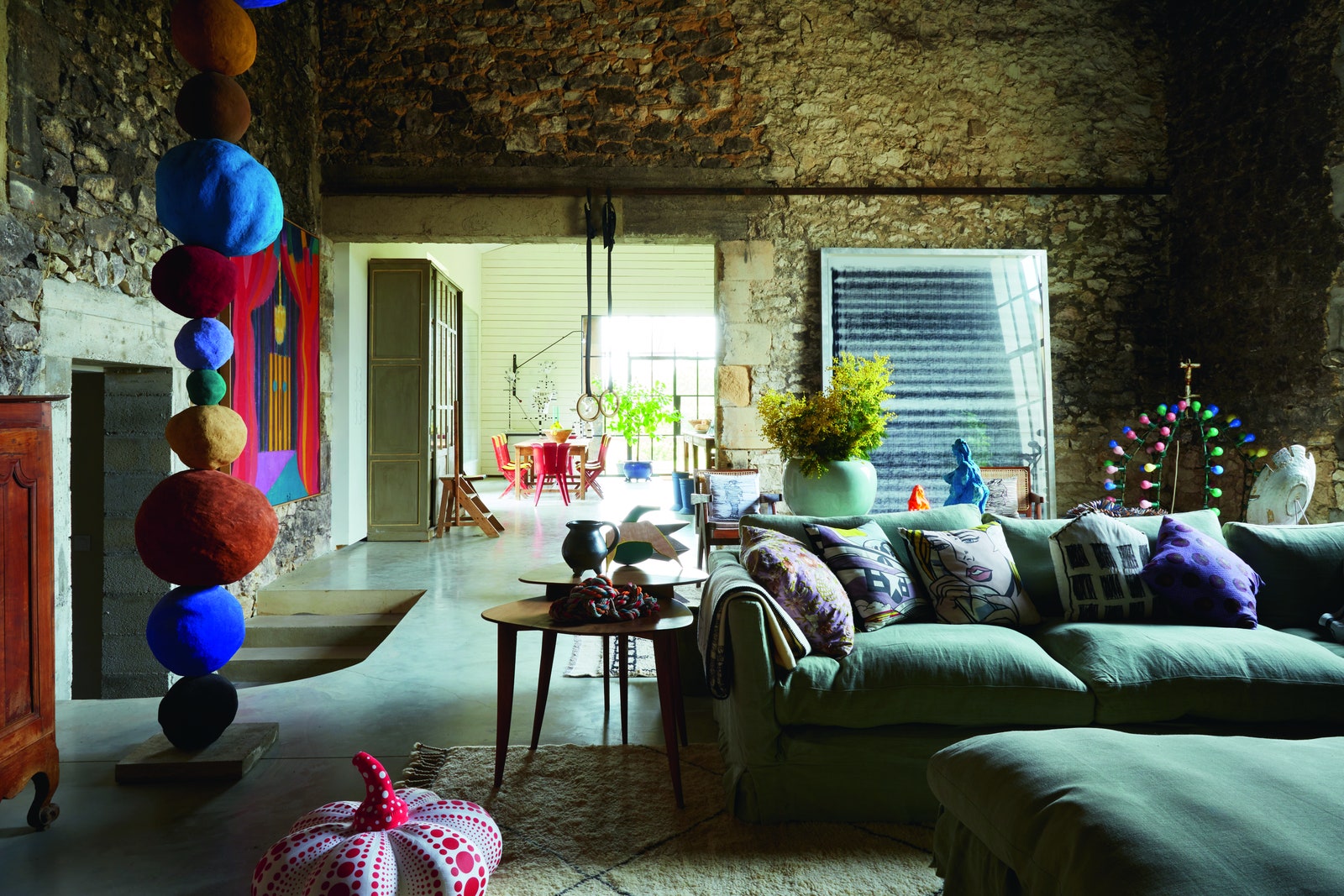 A living room with stonestacked walls and green sofa. To the left sands a colourful sculpture comprised of stacked...