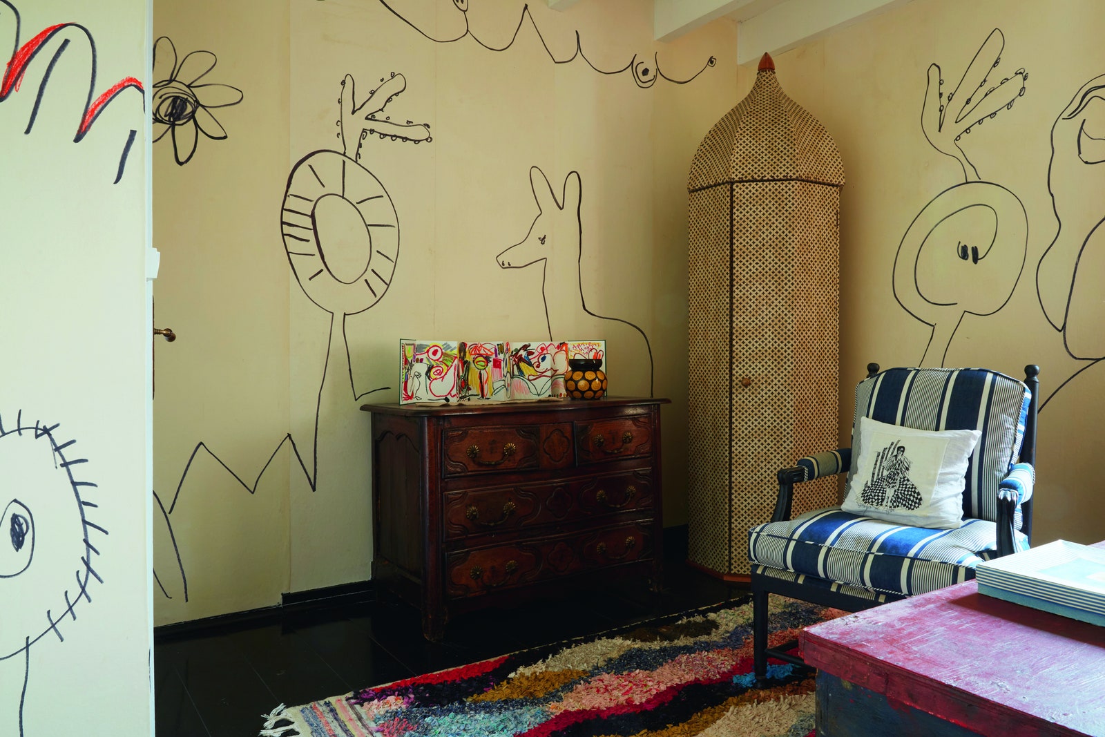 A room with children's drawings on the wall and a multicoloured rug on the black floor
